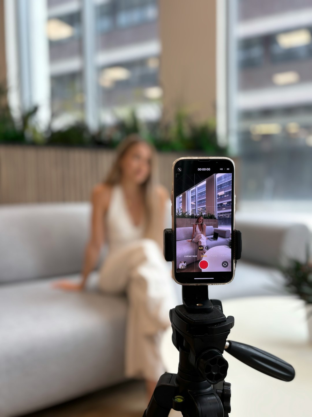 A woman sits on a couch while recording video content.