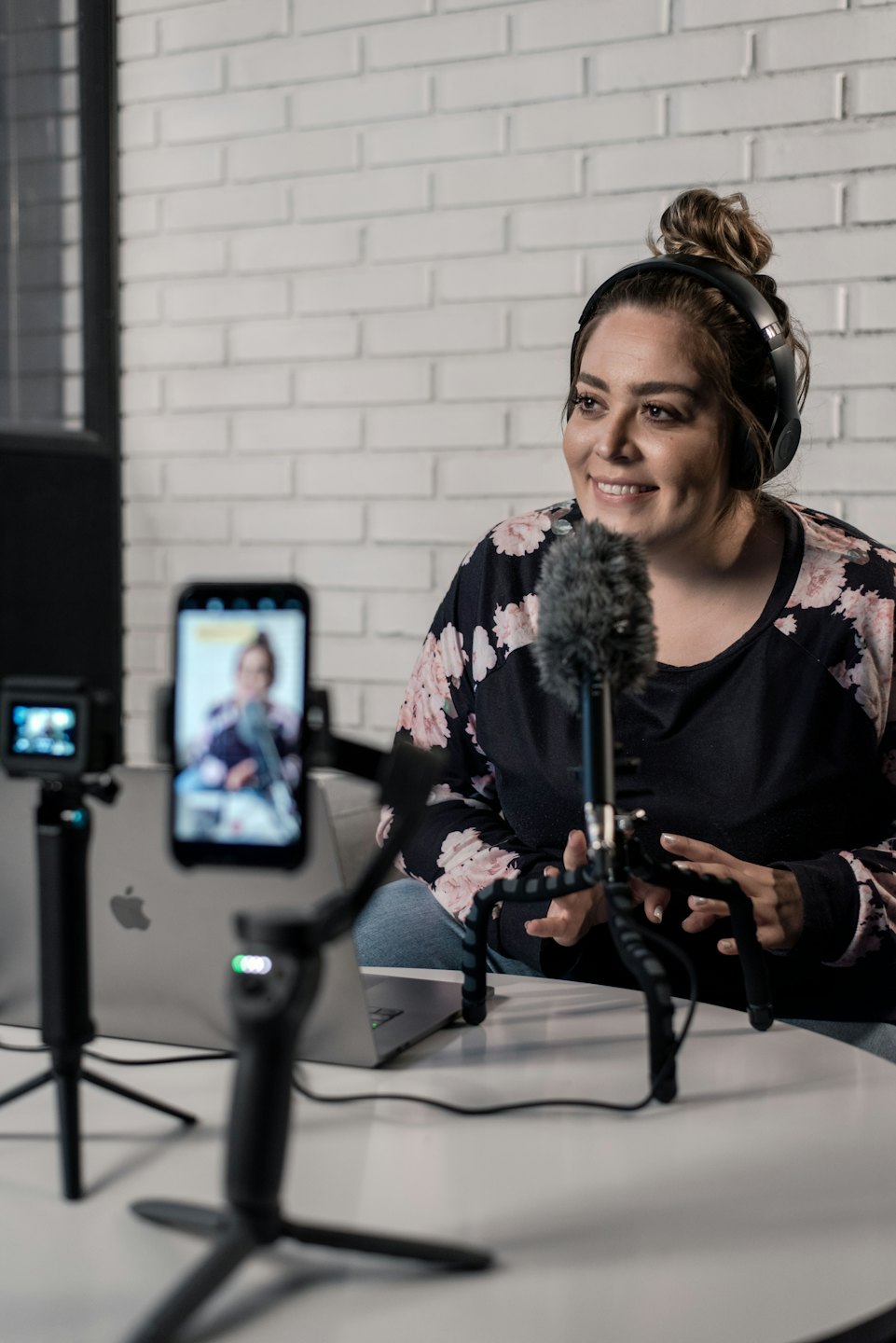 Woman records podcast at table with microphone and laptop.