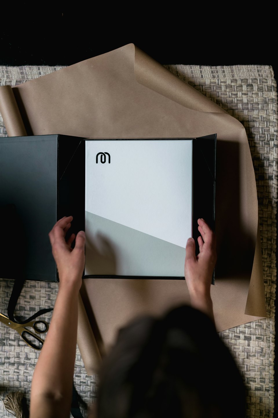 Hands opening a black box to reveal a white product with an 'm' logo.